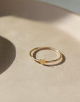 14k gold fill Tiny heart ring laid on a tan plate in the sunlight. This ring features a smooth band with a tiny heart. This ring is so cute stacked with any of the stacking rings at Token Jewelry.