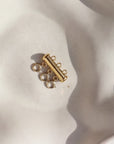 A gold necklace layering clasp with three necklace attachment points laid on a cream backdrop.