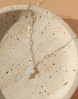 a mother of pearl white cross pendant on a 925 sterling silver chain, lying on a white ceramic dish