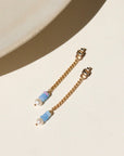 A 14k gold fill back drop with a dainty curb chain, with three opal gemstones and one mini pearl set at the bottom, the earrings are displayed on a cream backdrop in the sunlight.