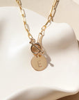 14k gold filled chain link necklace with a toggle clasp and monogrammed "E" flat disk charm, photographed on a white dish