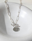 Sterling silver chain link necklace with a toggle clasp and monogrammed "B" flat disk charm, photographed on a white dish