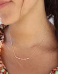 Model wearing a 14k gold-filled necklace with five coral tube gemstones and serpentine beads