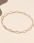 14k gold fill bangle with wave-like textured wire, displayed on a cream backdrop in natural sunlight.