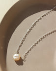 925 sterling silver freshwater pearl necklace laid on a peach colored plate. This necklace features the simple chain with the freshwater pearl wired in the middle.