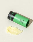 Green and black cylindrical container labeled 'Flower' with a dollop of yellow cream on a beige background