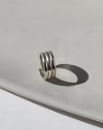 925 Sterling Silver Trinity ring spirals into three bands, photographed on a white sunlit ceramic dish. This ring features the look of the three layered band look but its only one ring.