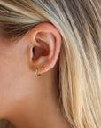 Close-up of an ear wearing a gold earring with blonde hair.