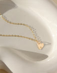 a dainty heart charm with an initial stamped on them, on a necklace chain, photographed on a ceramic dish