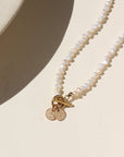 A fully beaded pearl toggle necklace with two 1/4" stamped disc with an "C" and a "A". The necklace is displayed on a cream back drop.