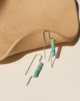 Sterling silver threaders with two turquoise tube shaped gemstones, the earrings are displayed on a cream backdrop