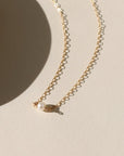 Gold chain necklace with a single pearl pendant on a beige background