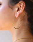 Hammered Paloma earrings taken a brunette model. These earrings feature a wire around 1/2 inch shaped like an oval, then followed by the other half of the oval that is hammered. Model is also wearing a thin gold chain also known as our Delaney chain.