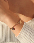 14k gold fill bold link chain Demi Alexandra Bracelet featuring two gold fill disks with a "B" and an "E", photographed on model wearing a white long sleeve t-shirt.