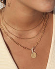 14k gold fill chain link necklace with a toggle clasp and monogrammed "E" flat disk charm, photographed on a model with brown hair, wearing gold jewelry, and pearl hoop earrings