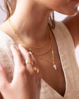 a mother of pearl white cross pendant on a 14k gold fill chain, photographed on a model wearing a cream linen vest and other 14k gold fill chain necklaces made by Token Jewelry