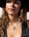 Sterling silver chain link necklace with a toggle clasp and monogrammed "B" flat disk charm, photographed on a model with long brown hair, wearing silver jewelry, a black denim vest, and a black cowboy hat