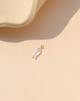 Mother-of-pearl fish charm with gold loop, photographed on a warm cream background beside a ceramic form.