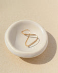A gold-colored band ring with a lightly hammered finish displayed on a white dish.