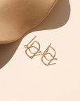 Curved 14k gold fill wire stud designed to wrap around the ear, displayed on a cream backdrop in natural sunlight