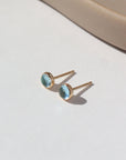4mm Blue Topaz gemstones set in a 14k gold fill bezel stud earring and placed on a white plate for display. Sold as a pair and perfect for single or double pierced ears.