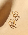 14k gold fill Mini Twist Earrings laid on a peach colored plate in the sunlight. These earring have a little twist giving the allusion that you have two piercings.