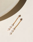 A 14k gold fill curb chain backdrop with three trillium pearls at the bottom of each chain, the backdrops are displayed on a cream display in the sunlight