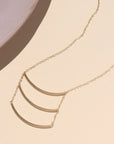 14k gold fill pendant necklace with three curved metal bars, displayed in natural sunlight