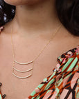 Model wearing a 14k gold fill pendant necklace with three curved metal bars