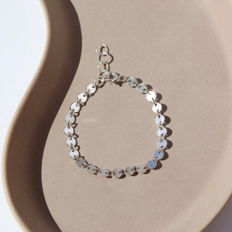 a sterling silver chain made up of small silver discs connected with small jump rings, laid on a ceramic plate