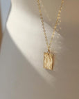 Rectangle 14k gold filled charm suspended from a delicate cable chain with clasp closure. Charm is hammered to a pretty shine and displayed on a white plate. Handmade by Token Jewelry in Eau Claire, WI Box Charm Necklace - Token Jewelry  Edit alt text