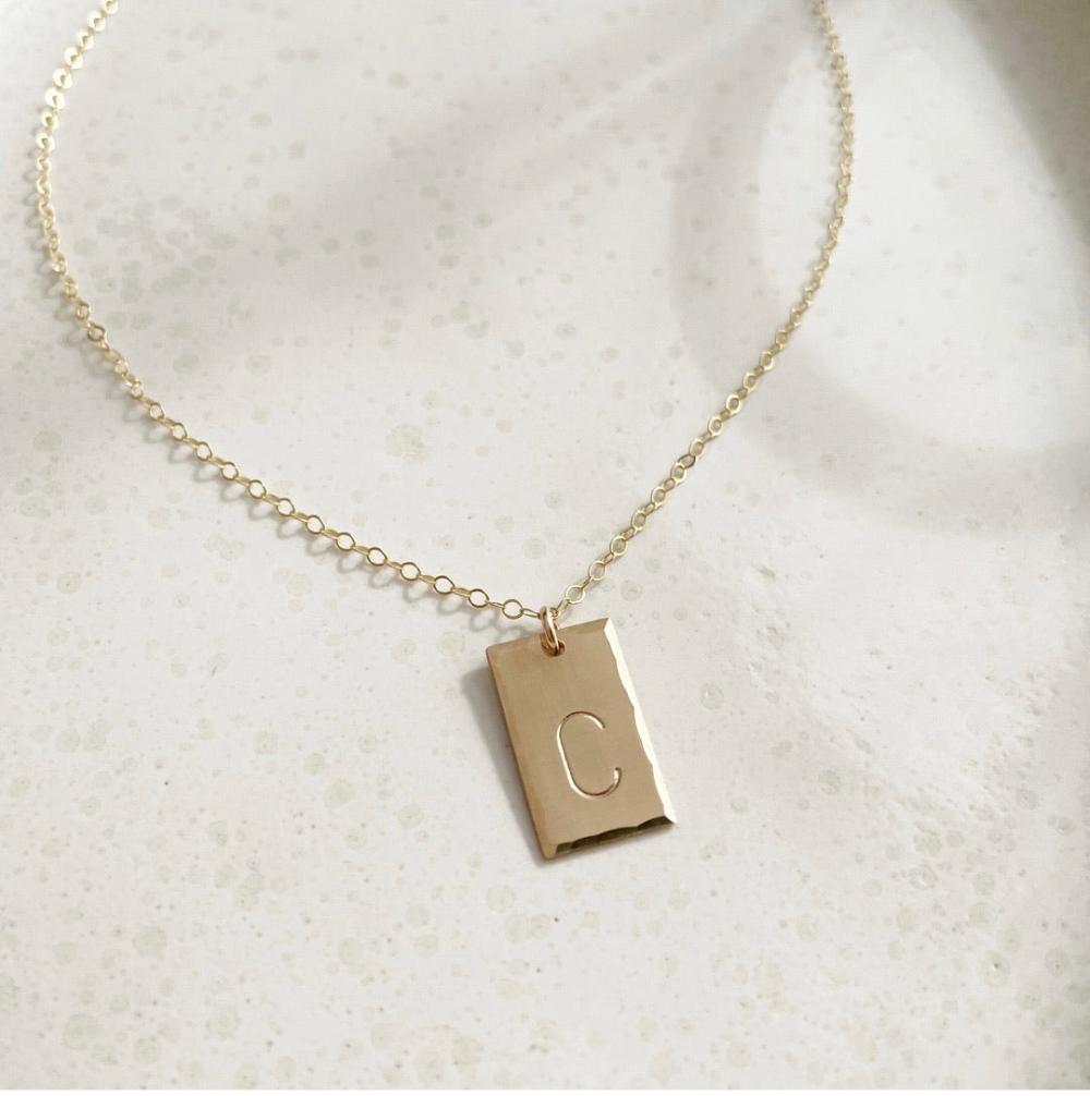 14k gold fill Everly Monogram Necklace placed on a white plate. Simple chain - Gold or Sterling Silver Rectangle Hammered edge - Monogrammed with letter - Jewelry near me - Eau Claire