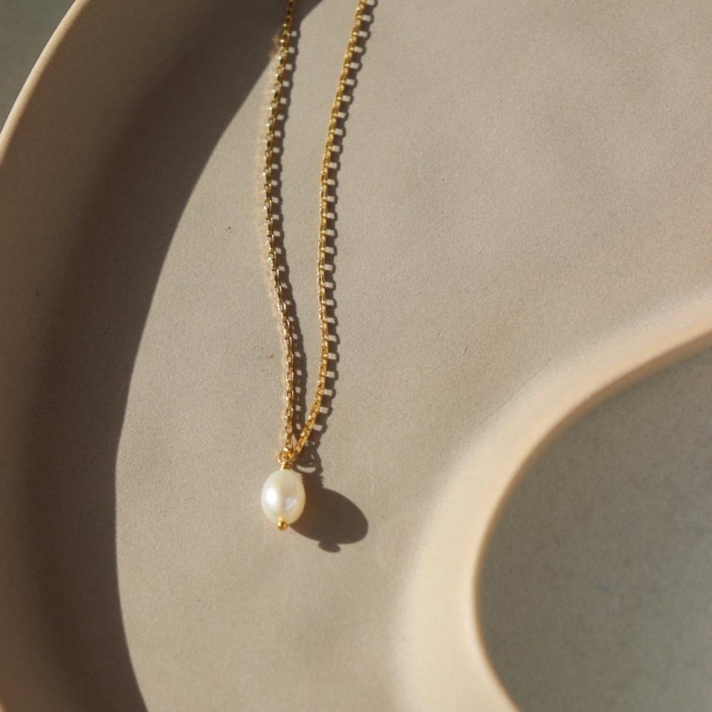 14k gold floating pearl necklace laid on a peach colored plate laying in the sunlight.