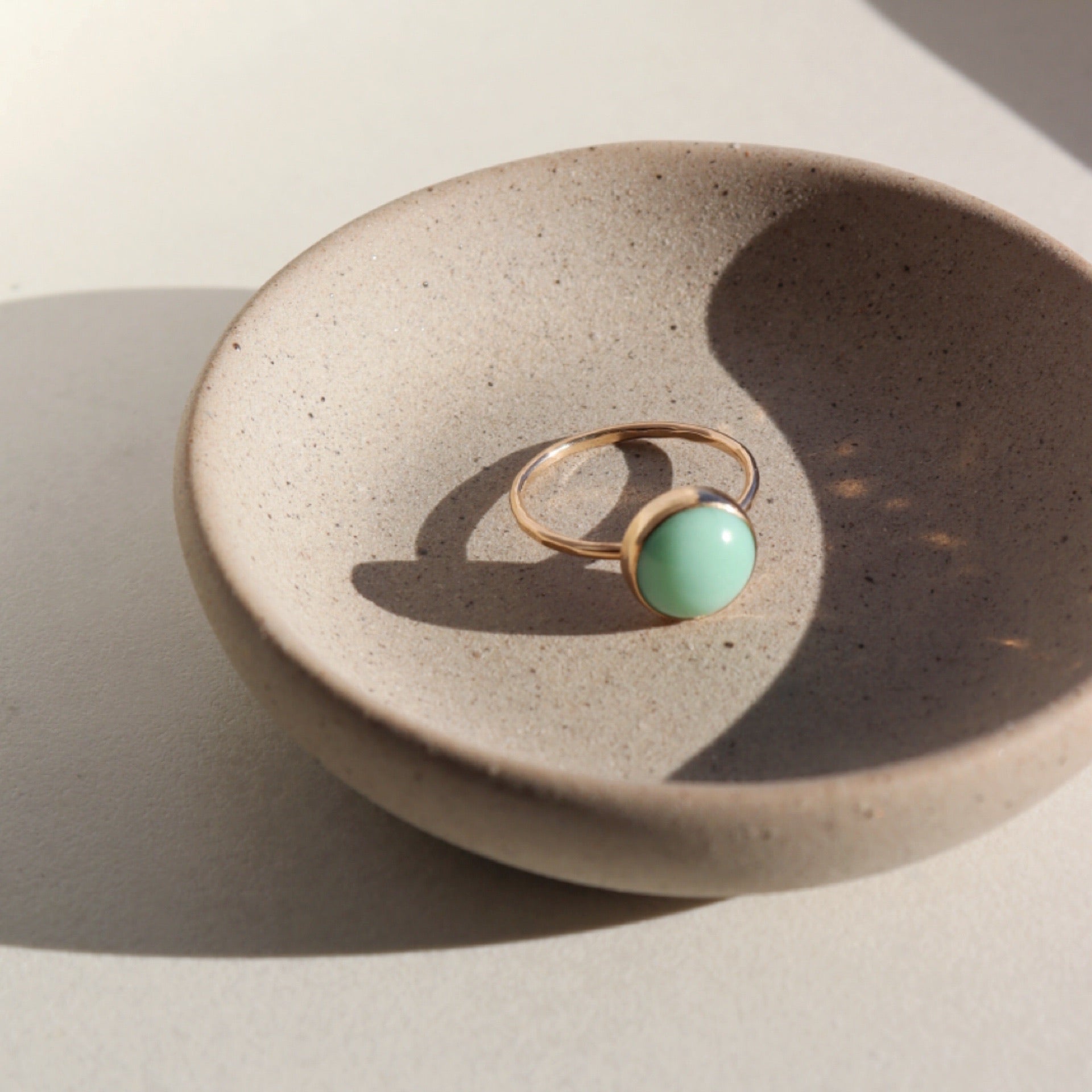 14k gold fill Lucky Ring placed on a gray plate in the sunlight. This Ring features the Chrysoprase gemstone.