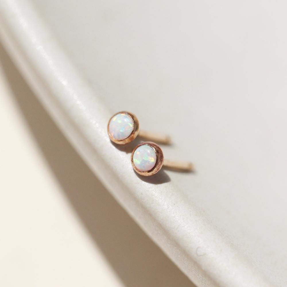 14k gold fill Petite opal studs laid on a tan plate in the sunlight. these earring feature a 3mm opal gemstone followed by a bezel ear post.