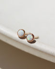 14k gold fill Petite opal studs laid on a tan plate in the sunlight. these earring feature a 3mm opal gemstone followed by a bezel ear post.