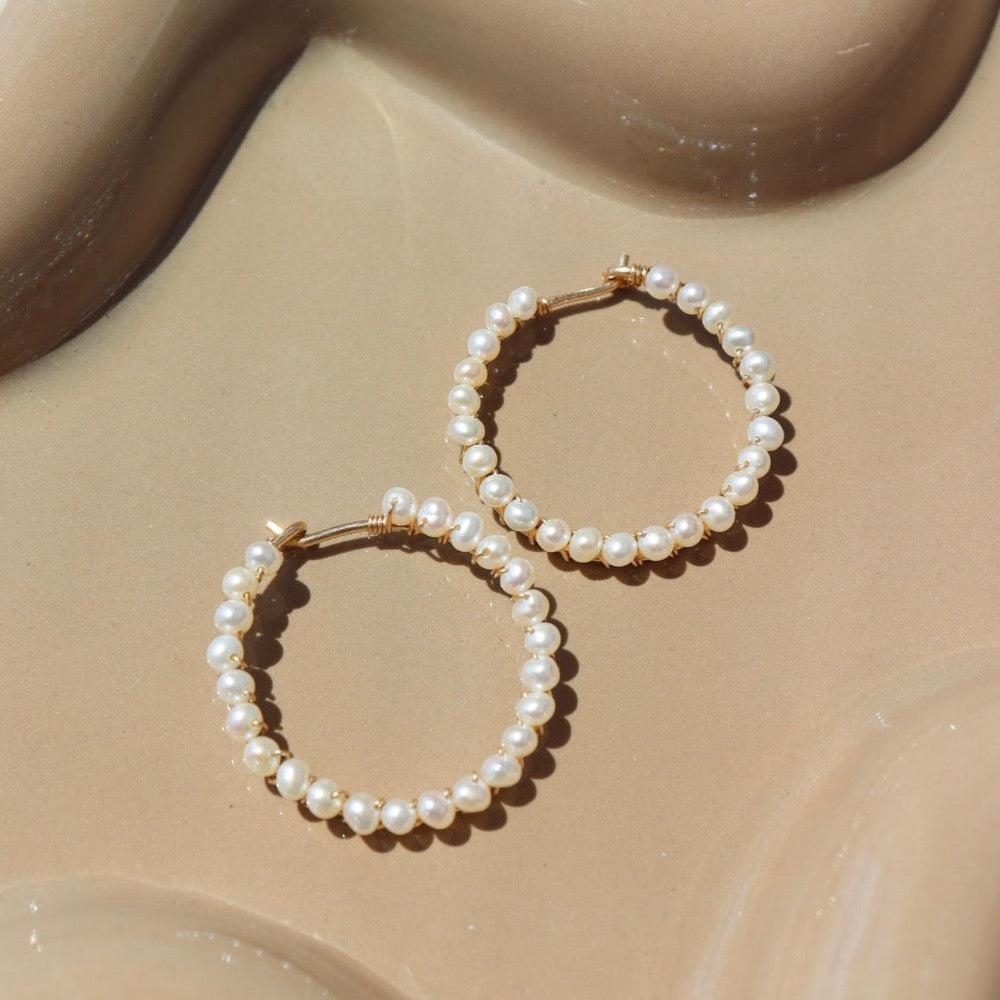 14k gold fill Pearl halo hoops laid against a tan plate in the sunlight.