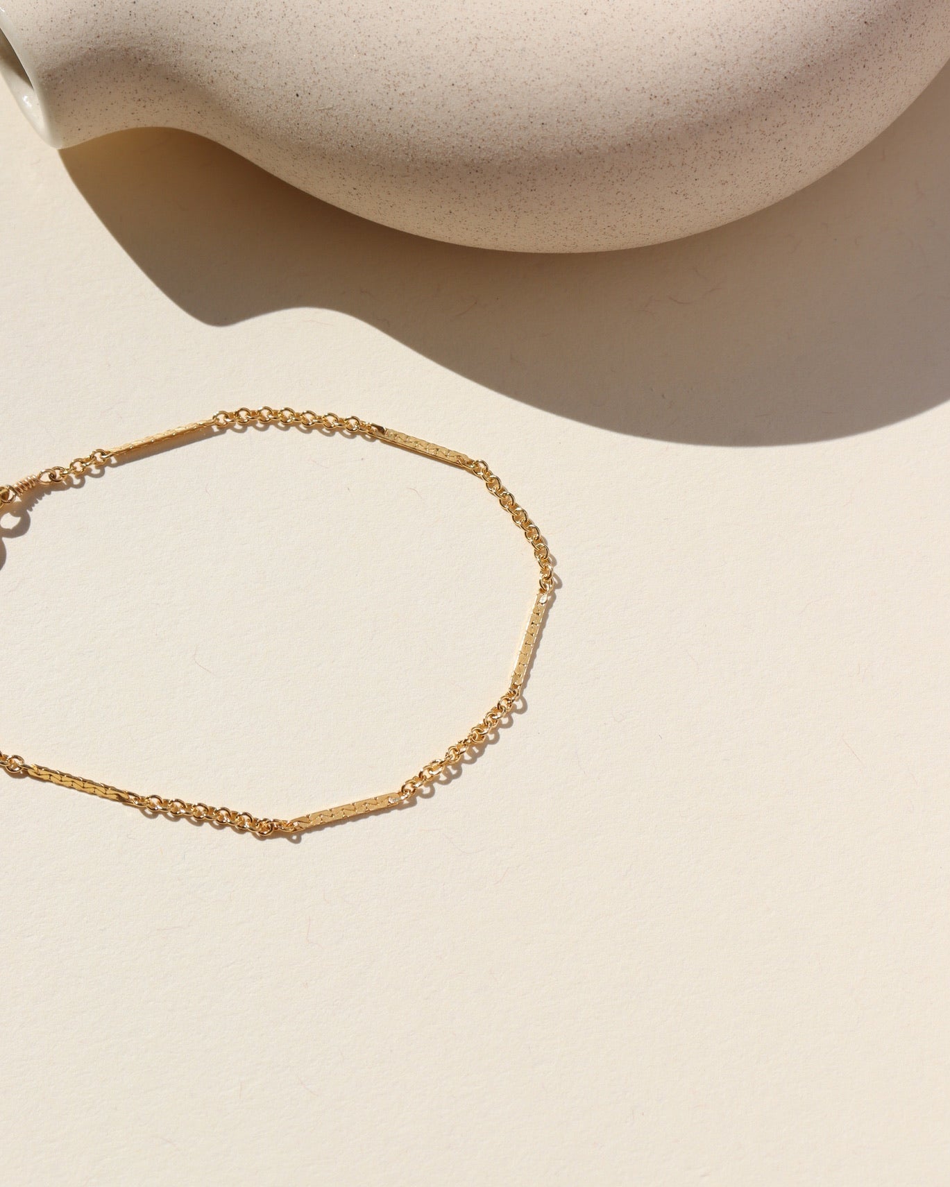 14k gold fill Sailor Bracelet featuring a bar and link dainty chain laid on a tan plate in the sunlight
