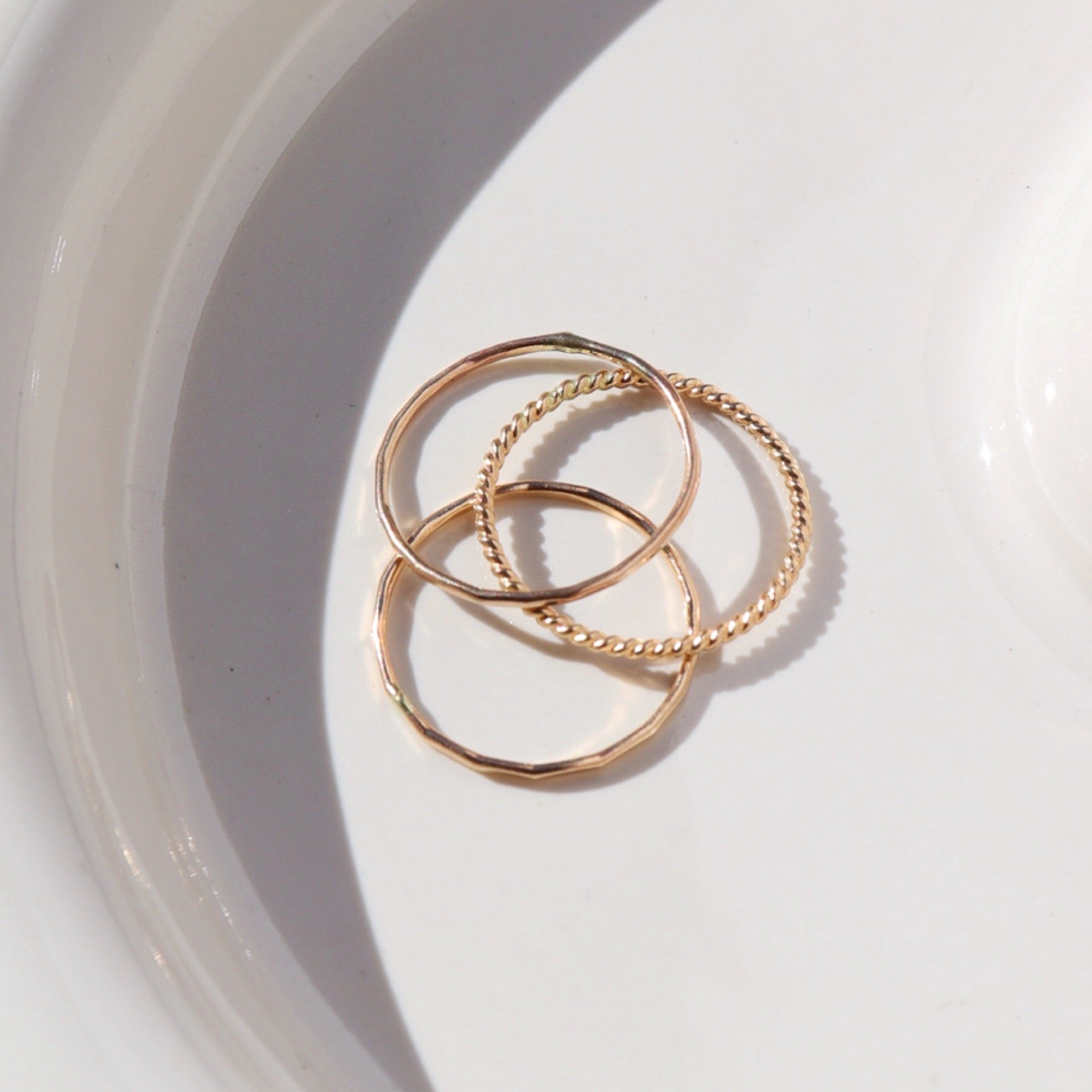 14k gold fill SoHo Ring Set placed on a white plate. This Ring set highlights each one of our go to stacking rings including the stacking ring, spiral ring, and sequins ring. These rings are made to live in made to wear everyday. 