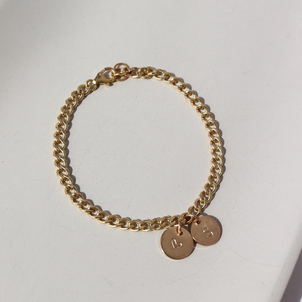 14k gold fill bold link chain Demi Alexandra Bracelet featuring two gold fill disks with a heart and an "S", photographed on a white tabletop