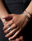 three stacked everyday cuffs from token jewelry, made with 925 sterling silver, photographed on a model wearing silver rings and a black denim skirt