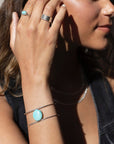sterling silver double wire cuff bracelet featuring a large turquoise stone wired to the middle. Photographed on a model's arm wearing a black denim skirt, black cowboy boots, and silver rings