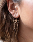 delicate 14k gold fill bow earring on a hook hand made by Token Jewelry, photographed on a model