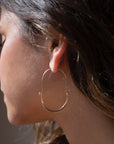 Model wearing Hammered Paloma Hoops. These earrings feature a wire around 1/2 inch shaped like an oval, then followed by the other half of the oval that is hammered.