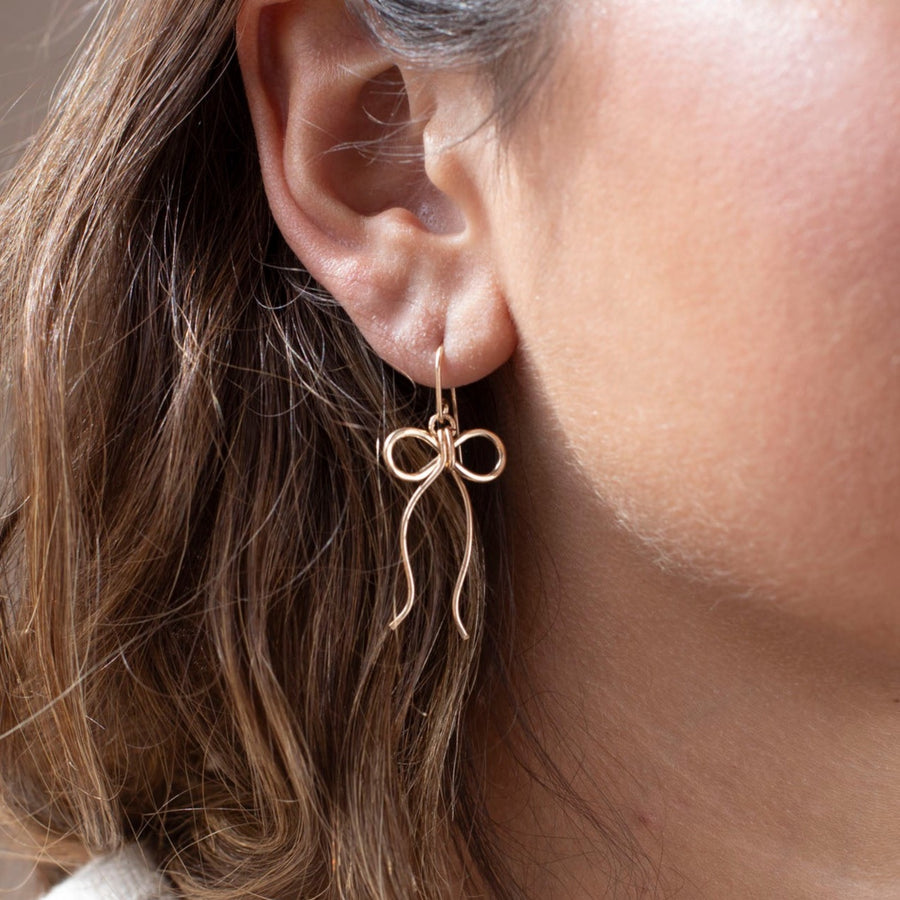 delicate 14k gold fill bow earring on a hook hand made by Token Jewelry, photographed on a model