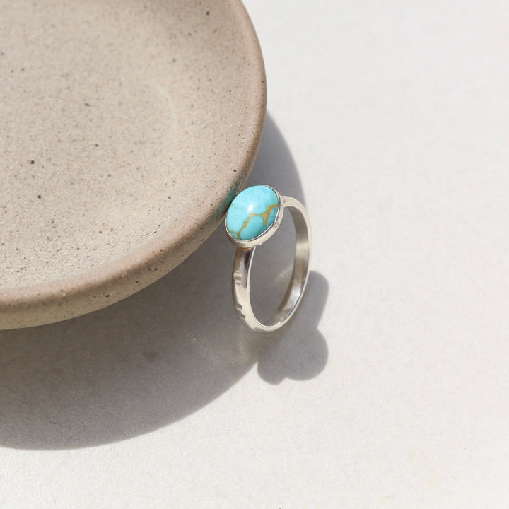 Sterling silver canyon ring with turquoise stone resting on a stoneware dish.
