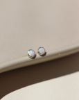 14k gold fill Petite opal studs laid on a tan plate in the sunlight. these earring feature a 3mm opal gemstone followed by a bezel ear post.