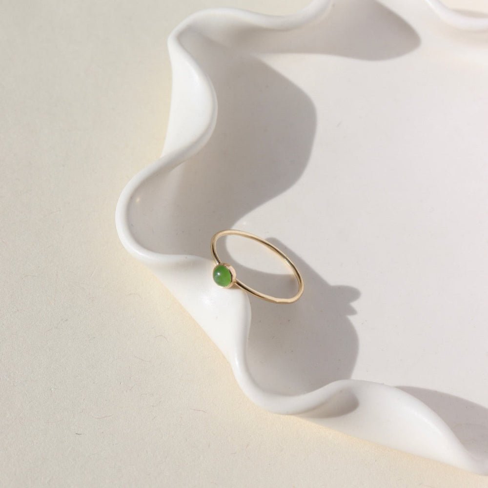 4mm Jade Gemstone Ring set in a 14k gold fill bezel with simple hammered ring band. The Ring is sitting on a white ceramic plate.