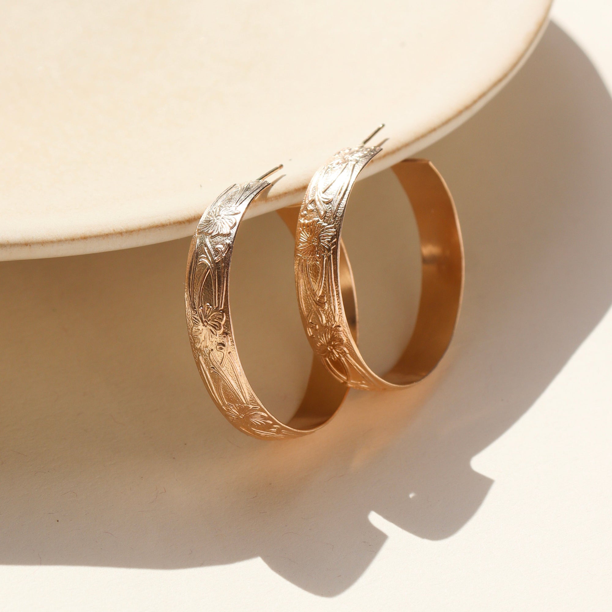 14k gold filled florence hoops resting on a stoneware plate in the sunlight