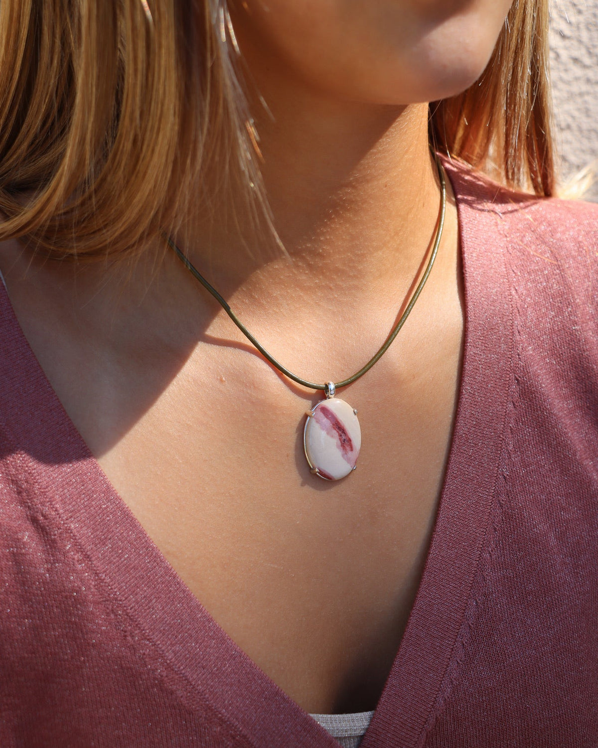 A close-up lifestyle shot of a woman wearing a gold chain necklace with a white and pink striped shell pendant.